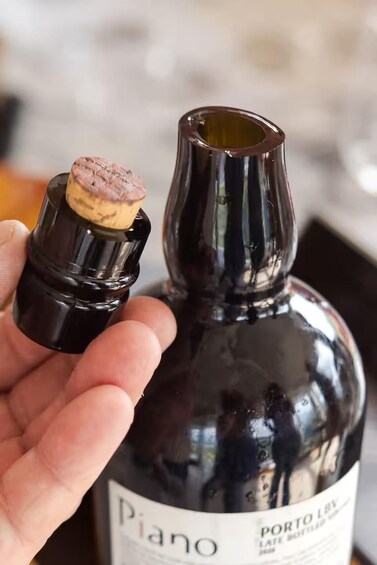 A hand holding a wine bottle with a cork. 2