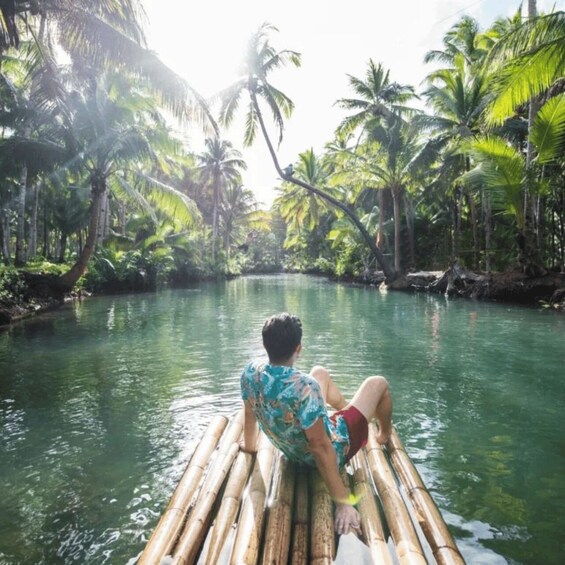 A person sitting on a bamboo raft in a river surrounded by palm trees. 3