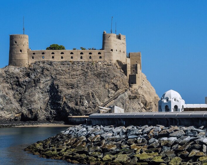 A coastal castle with two towers, a white dome, and a rocky shoreline. 4