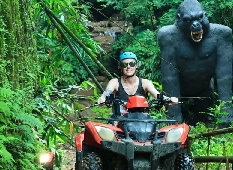 A person on a red ATV in a forest with a large gorilla statue. 4
