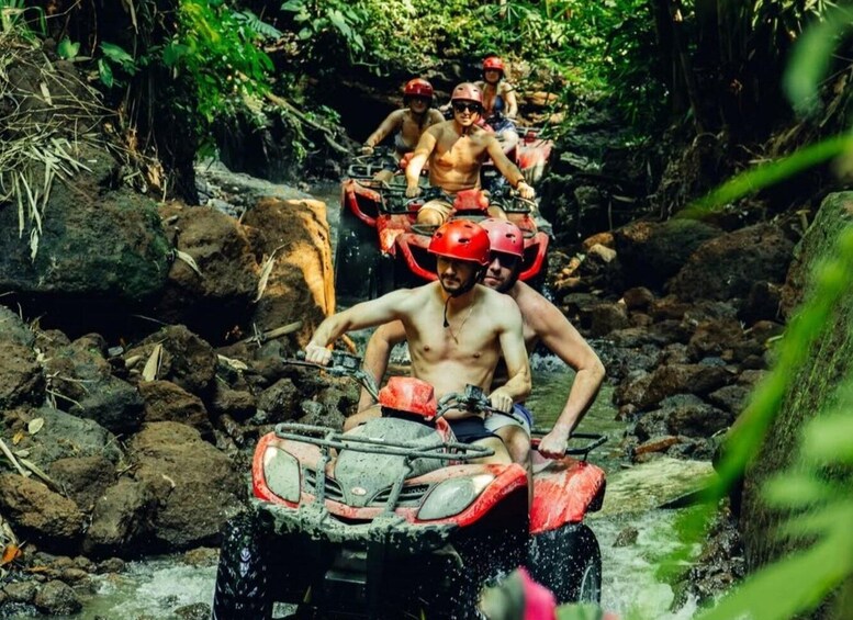 A group of people on an ATV navigating a rocky stream in a forested area. 2
