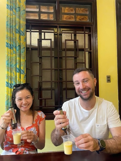 Two people sitting at a table with drinks, a window with a geometric pattern, and curtains with a leaf pattern. 4