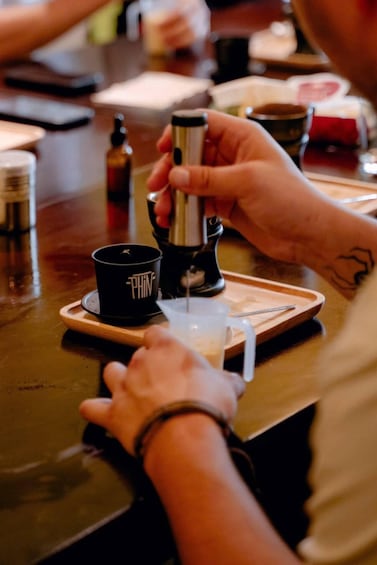 A person pouring a liquid from a bottle into a cup on a wooden tray. 3