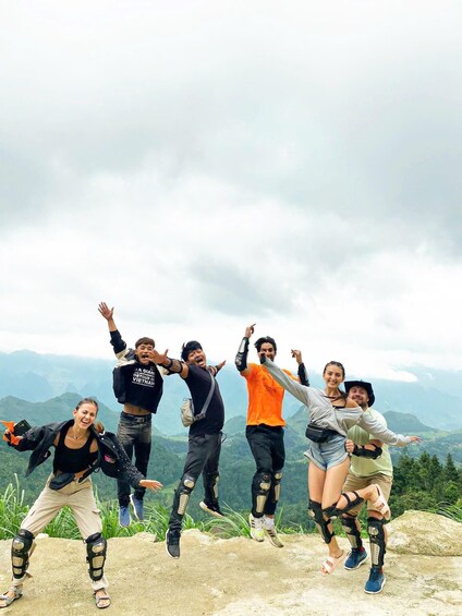 A group of people jumping on a rocky outcrop with a mountainous landscape in the background. 3