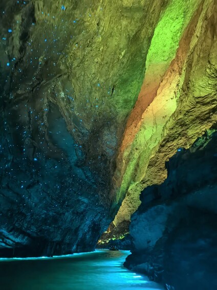 A cave with a water stream, illuminated by green and blue lighting, and speckled with blue particles. 2