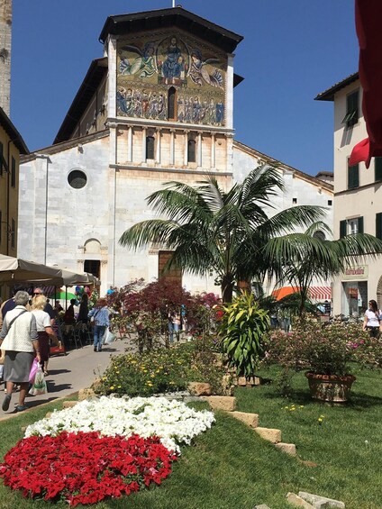 A historic building with a detailed mural, surrounded by a well-maintained garden with flowers and palm trees. 1