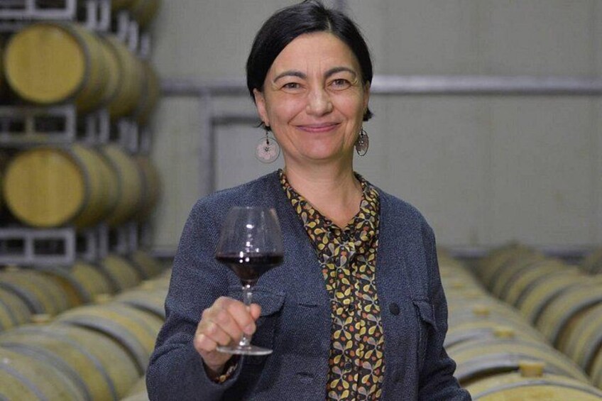 A person holding a wine glass in a cellar with rows of wine barrels. 2