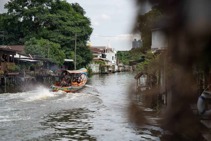 A colorful boat speeding through a narrow waterway flanked by buildings and trees. 2