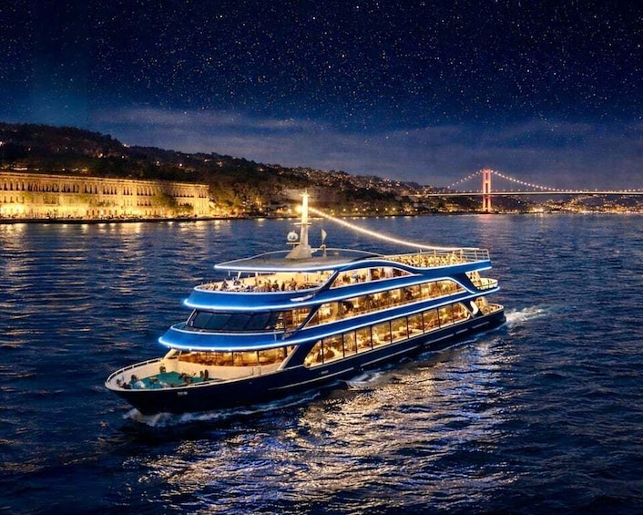 Een grote, verlichte rivierboot met meerdere dekken, vaart onder een sterrenhemel met een brug op de achtergrond. 1