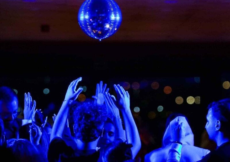 Een discobal hangt aan het plafond in een zwak verlichte ruimte, mensen doen hun handen omhoog. 3