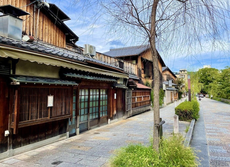 A traditional wooden building with a tiled roof, a stone-paved street, and a tree in the foreground. 3