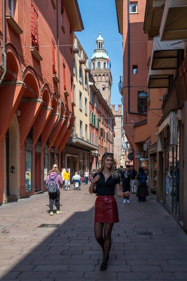 A pedestrian street lined with historic buildings, a tower in the background, and people walking. 2