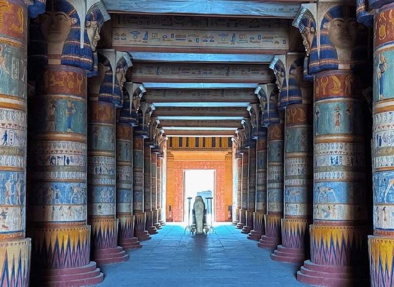 A corridor with hieroglyphs on columns and a statue in the distance. 2