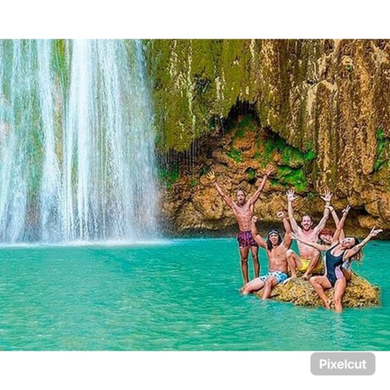 A group of people enjoying a waterfall in a clear blue pool. 1
