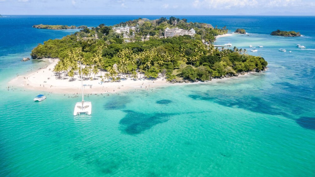 An island with a beach, clear turquoise waters, and a boat anchored near the shore. 5