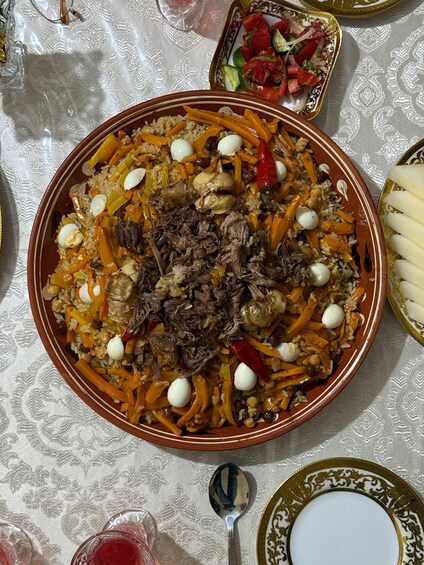 A large, ornate bowl filled with a rice dish, garnished with carrots, chickpeas, and eggs, on a table with a lace tablecloth. 3