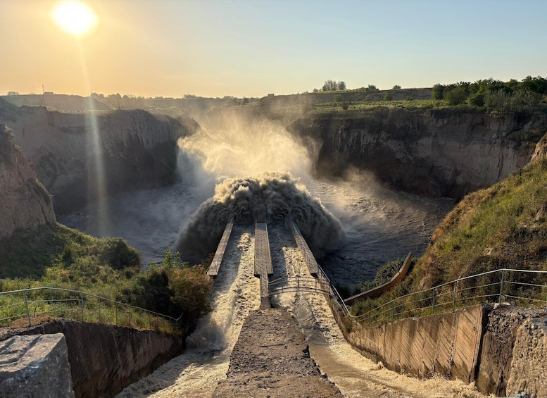 A dam with water cascading down a spillway, surrounded by rocky terrain and vegetation. 1
