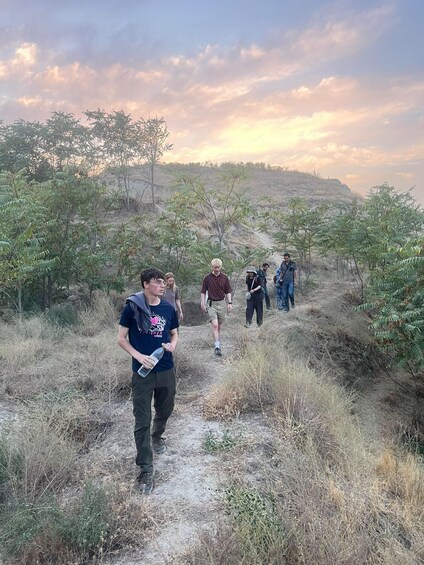 A group of people hiking on a dirt trail surrounded by dry grass and sparse trees. 5