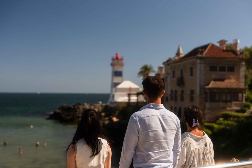 A coastal scene with a lighthouse, a building with a red roof, and people overlooking the ocean. 5