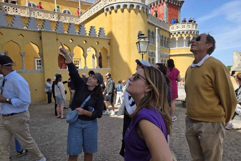 A historic yellow building with arches and a balcony, surrounded by tourists. 3