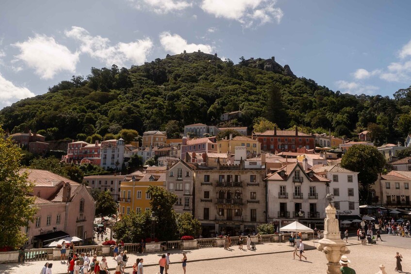 A town with colorful buildings, a hill with trees, and a fountain in the square. 2