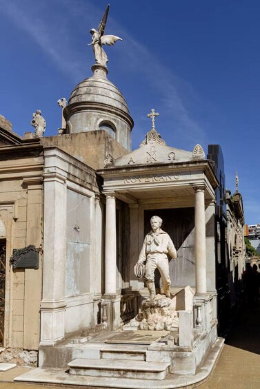 A statue of a man in a white robe holding a book, standing on a pedestal with steps leading up to a building with a dome and a cross on top. 4