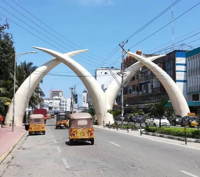 A street with a distinctive white archway, vehicles, buildings, and power lines. 1