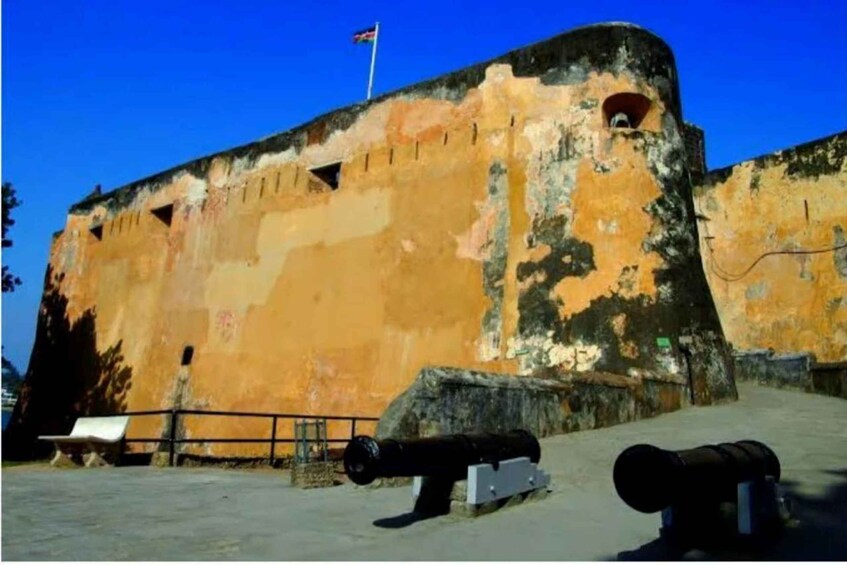 A weathered fort with cannons, a flag, and a bench. 5
