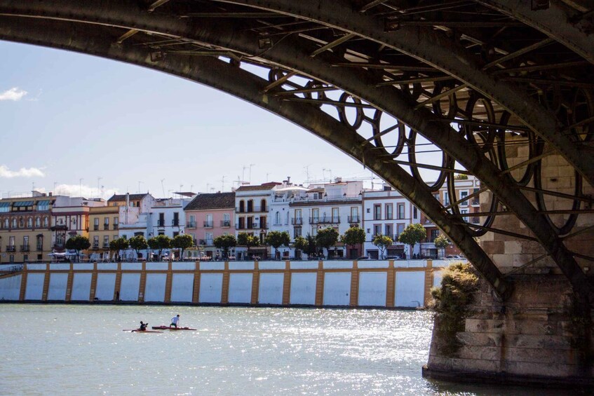 A bridge with a metal structure, a river, and buildings along the riverbank. 3