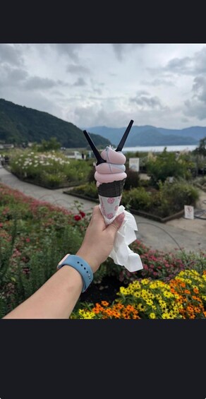 A hand holding a cone with a drink and a straw, with a mountainous landscape in the background. 5