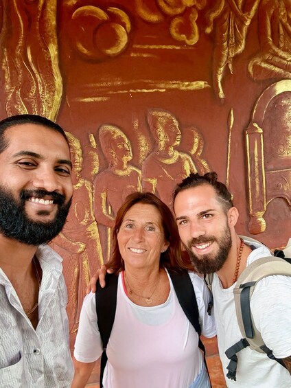 Three people standing in front of a wall with golden carvings. 5