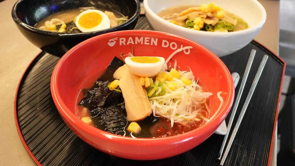 A red bowl of ramen with a boiled egg, corn, and seaweed on a black tray. 5