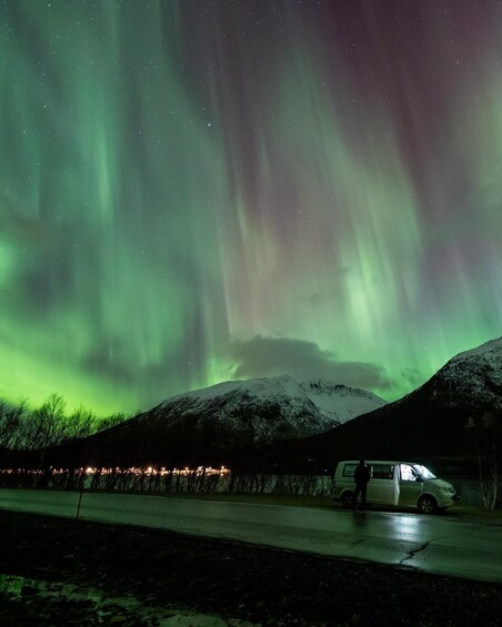 The Northern Lights over a snowy landscape with a van parked on the roadside. 3