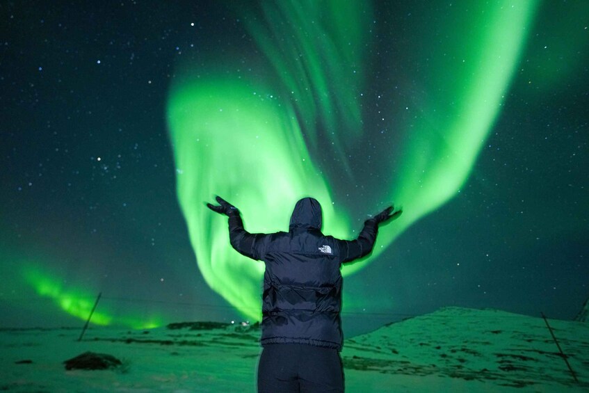 Una persona de pie con los brazos extendidos bajo las auroras boreales. 1