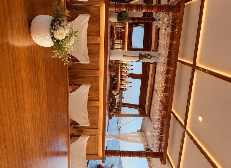 A restaurant interior with wooden furniture, white tablecloths, and a bar area with bottles. 2
