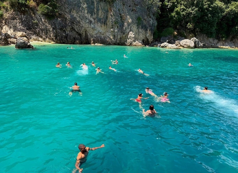 A group of people swimming in clear turquoise water surrounded by rocky cliffs and greenery. 4