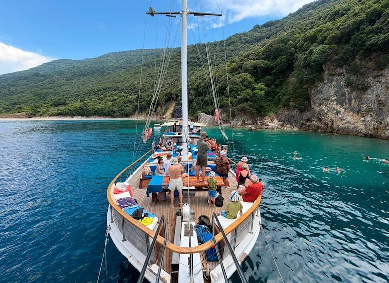 A sailboat with passengers enjoying the sea, surrounded by lush green hills and clear waters. 5