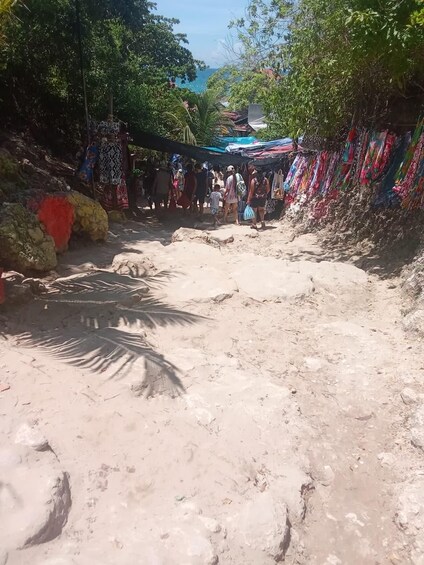 A sandy path with colorful fabrics hanging on the sides, leading to a beach area. 2