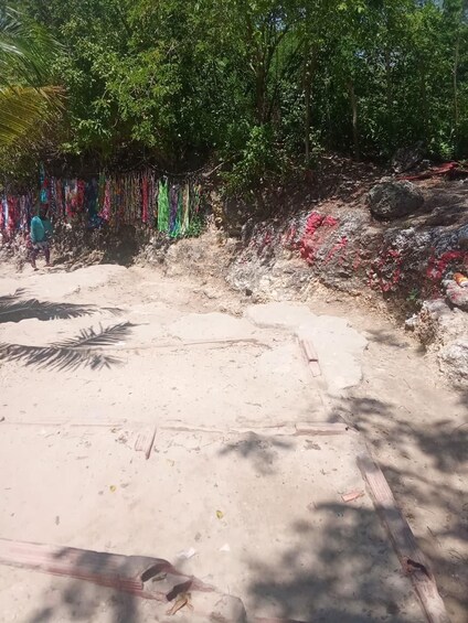 A sandy beach with colorful decorations hanging from trees, a rocky outcrop, and a wooden structure. 5