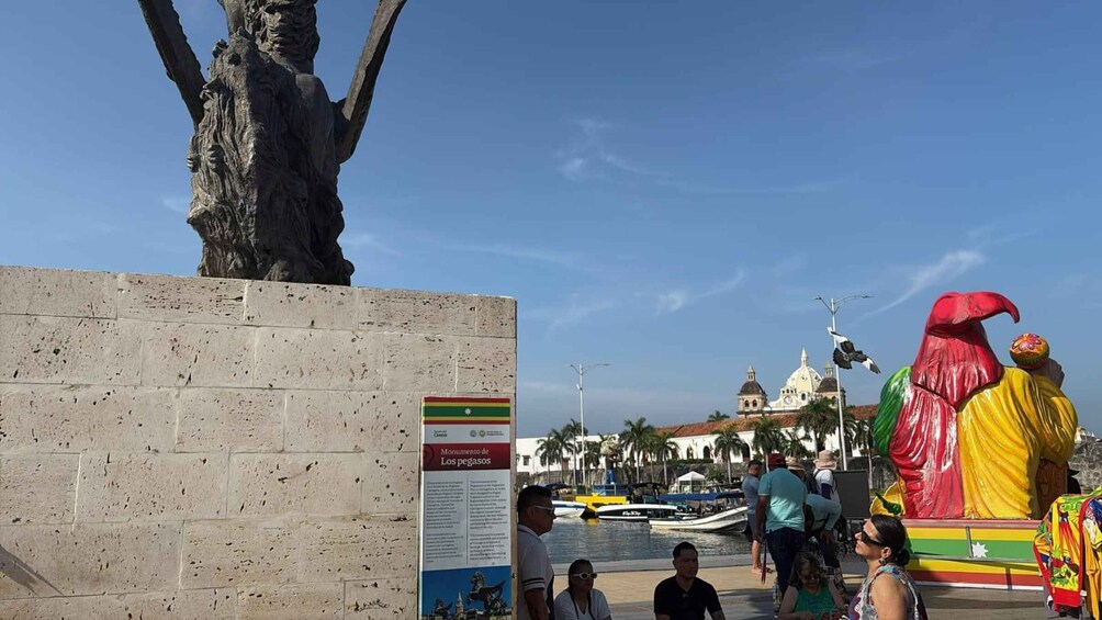 A statue of a figure with a red hat, a large tree, and a building with domes in the background. 4