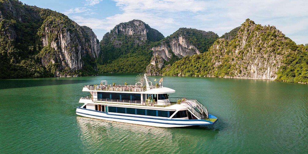 A white and blue riverboat on a calm river surrounded by lush green mountains. 1