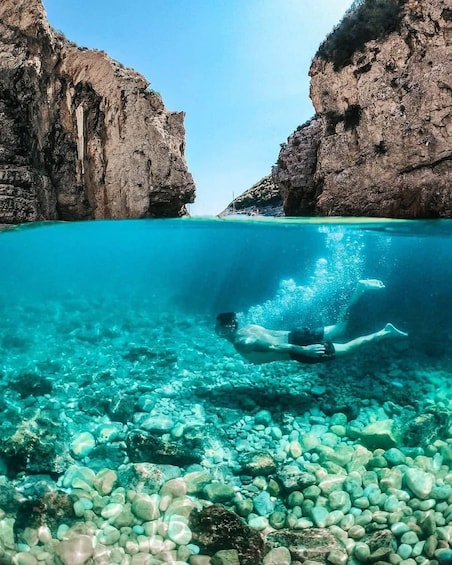 A person swimming underwater between rocky cliffs with clear turquoise water. 2