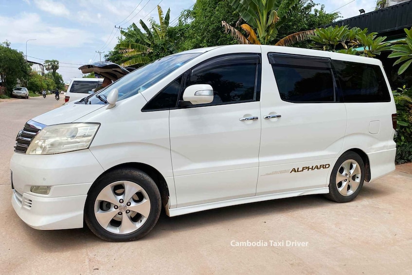 A white ALPHARD van parked on a street with greenery and a building in the background. 2