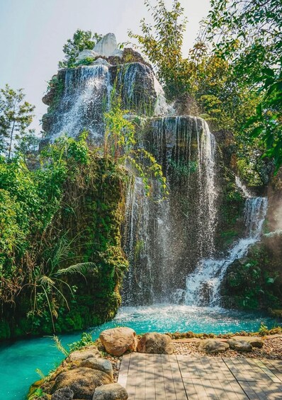 A waterfall cascading over rocks into a turquoise pool, surrounded by lush greenery. 2