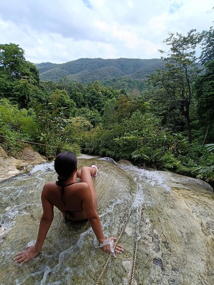 A person sitting on a rock by a waterfall in a forested area. 5