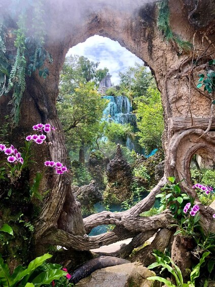 A natural archway with a waterfall and vibrant purple flowers. 1