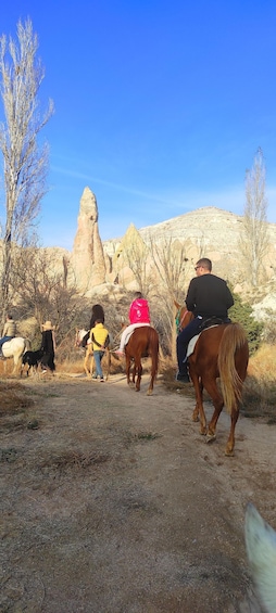 A group of people riding horses on a dirt path with a rocky mountain in the background. 2