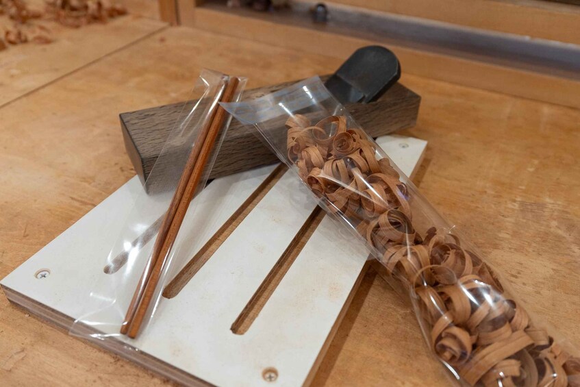 A woodworking tool, a piece of wood, and a plastic bag with wood shavings on a workbench. 1
