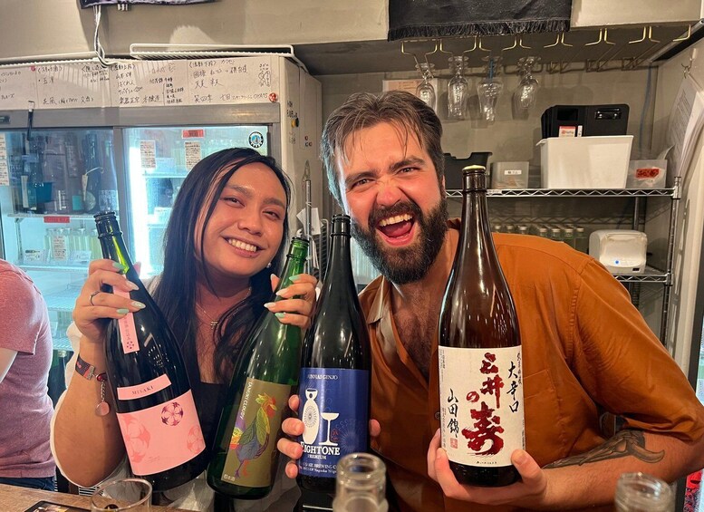 Three people holding wine bottles in a bar with shelves of glasses and bottles in the background. 1