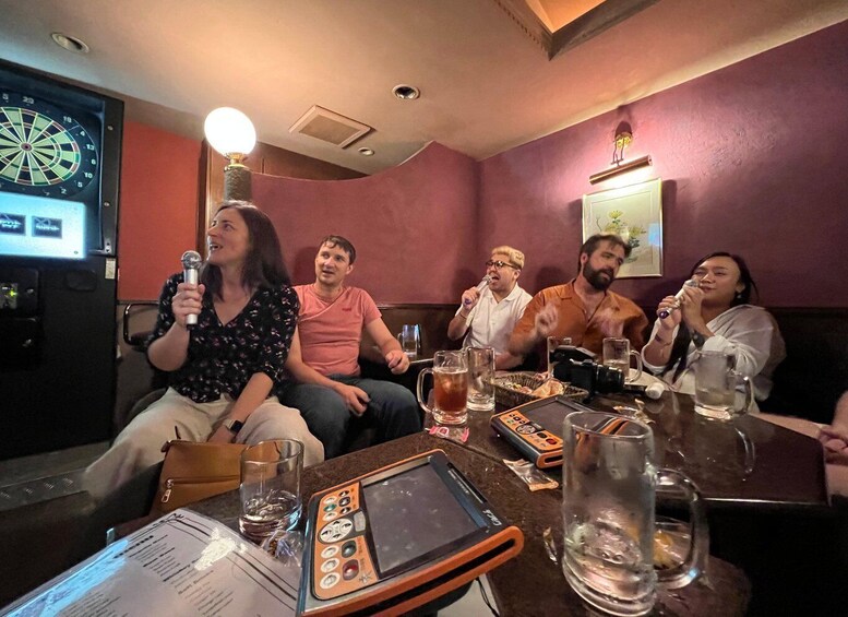 A group of people seated at a table in a restaurant with a dartboard and a television screen in the background. 4